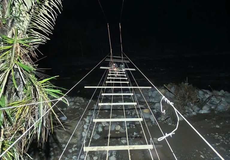 Tim gabungan dari Vertical Rescue dan Yon TP 836 membangun jembatan gantung di Lhok Sanding, Kecamatan Meurah Dua, Kabupaten Pidie Jaya, Provinsi Aceh, Minggu (22/2/2026).  Sungai Meureudu yang membelah Kabupaten Pidie Jaya, Provinsi Aceh, merupakan sungai induk (main stem) bagi sejumlah anak sungai (tributary) sebelum bermuara di perairan Selat Malaka. Karakteristik geografis ini membuat wilayah hilir sangat rentan saat hulu dilanda hujan lebat berdurasi lama. Puncaknya pada akhir November 2025 lalu, fenomena Siklon Senyar memicu curah hujan ekstrem yang menyebabkan debit air meluap drastis melampaui kapasitas sungai.  Banjir kiriman tersebut tidak hanya membawa massa air, tetapi juga material destruktif berupa potongan kayu, sampah, pasir, hingga bebatuan besar yang menghantam infrastruktur vital, termasuk memutus jembatan penyeberangan di Gampong Lhok Sanding, Kecamatan Meurah Dua.  Pasca-penanganan darurat, pemerintah kini berfokus pada fase pemulihan infrastruktur demi mengembalikan konektivitas warga yang sempat lumpuh total. Hingga hari Minggu (22/2), pembangunan kembali akses tersebut diwujudkan melalui proyek strategis jembatan gantung yang merupakan hasil kolaborasi solid antara tim ahli dari Vertical Rescue Indonesia dan prajurit Batalyon Infanteri Teritorial Pembangunan 836/Brahma Yodha (Yonif TP 836/BY).  Dengan dukungan penuh material bangunan dari Badan Nasional Penanggulangan Bencana (BNPB), tim gabungan ini terus berjibaku siang dan malam guna memastikan pembangunan berjalan sesuai target, mengingat peran jembatan ini sangat krusial dalam memulihkan roda ekonomi dan memangkas jarak tempuh warga.  Saat ini, akumulasi progres fisik pembangunan secara keseluruhan telah mencapai 65 persen. Secara teknis, sejumlah tahapan utama telah berhasil dituntaskan hingga 100 persen, meliputi pengeboran besi palang, pembentangan enam sling utama (atas dan bawah), mobilisasi material batu dan pasir ke titik A dan B, serta pengecatan dasar atau meni pada gapura di kedua sisi jembatan.***(Foto: Ekobisnis.com/Dok BNPB)